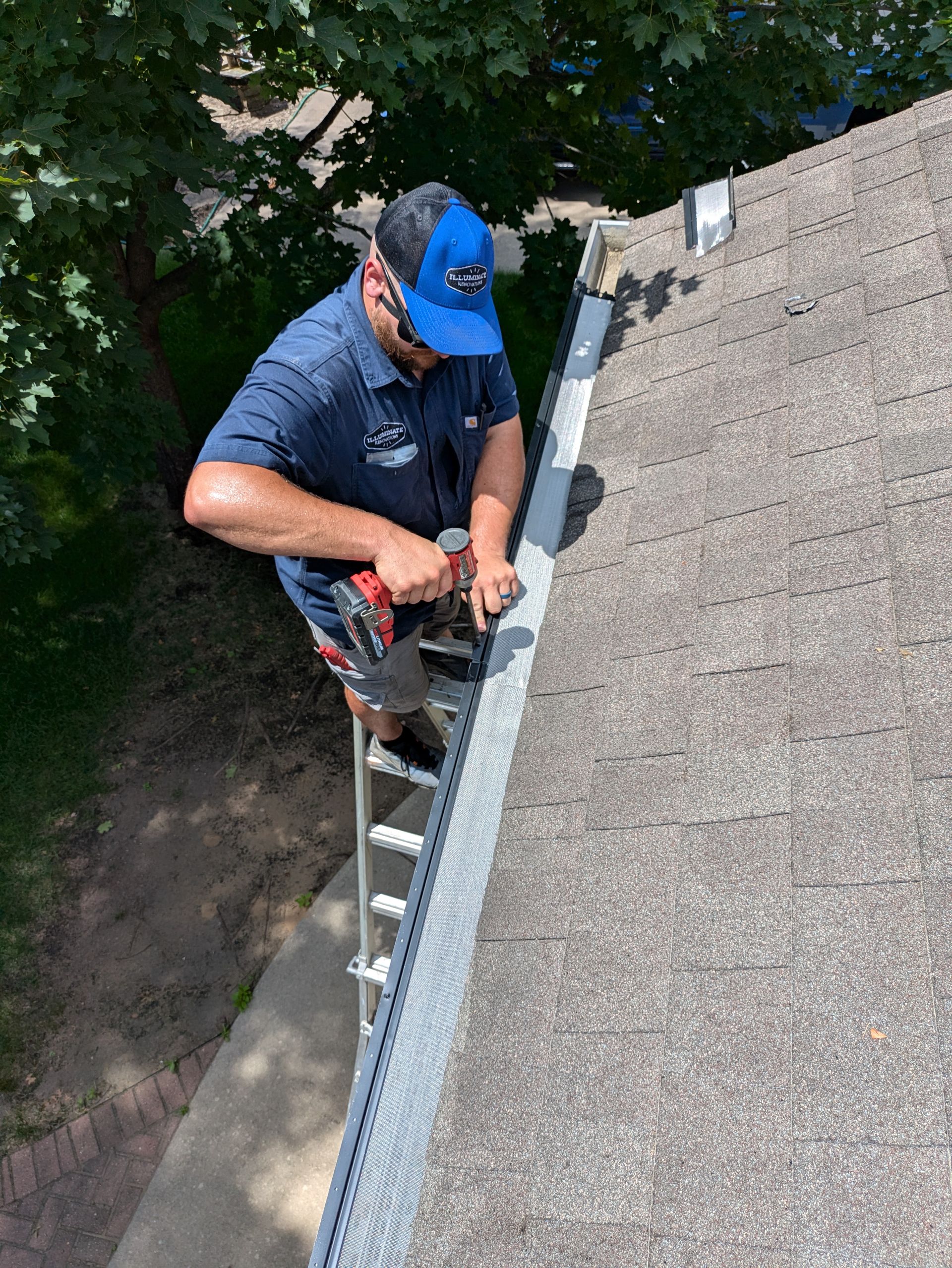 A man is standing on a ladder fixing a gutter on a roof.