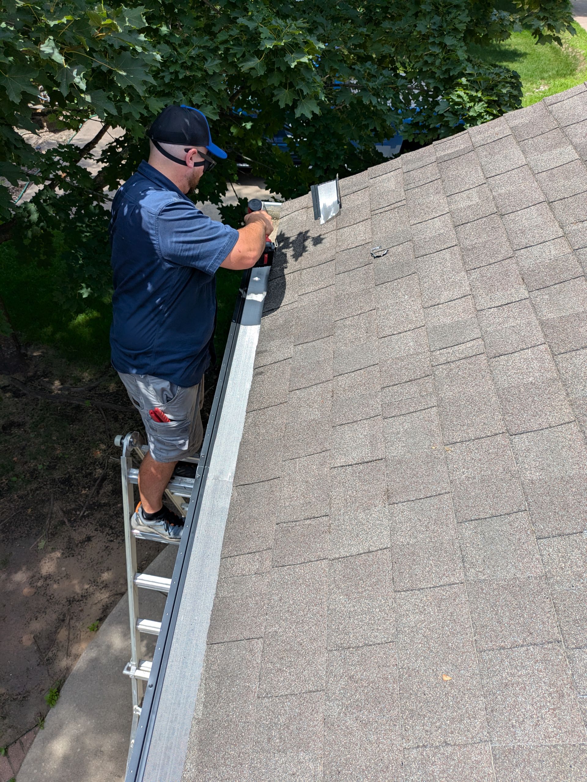 A man is standing on a ladder fixing a gutter on a roof.