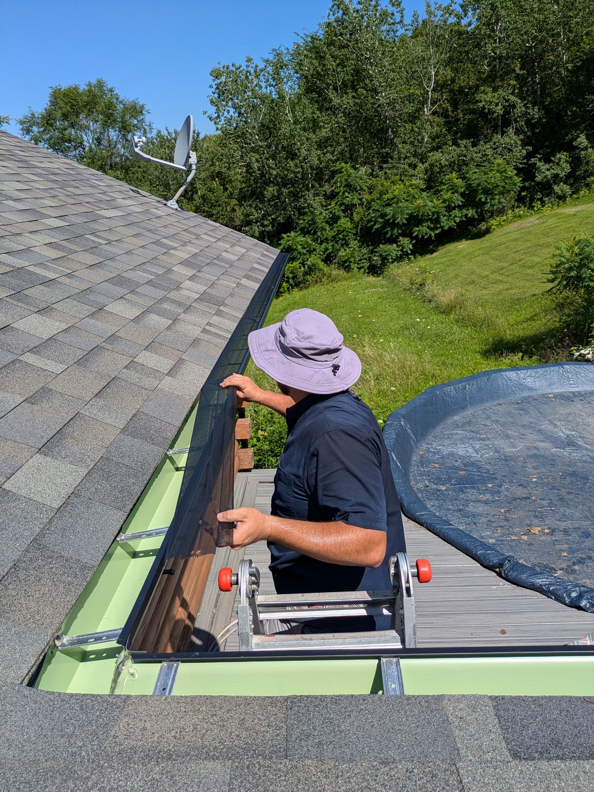 A man is standing on a ladder fixing a gutter on a roof.