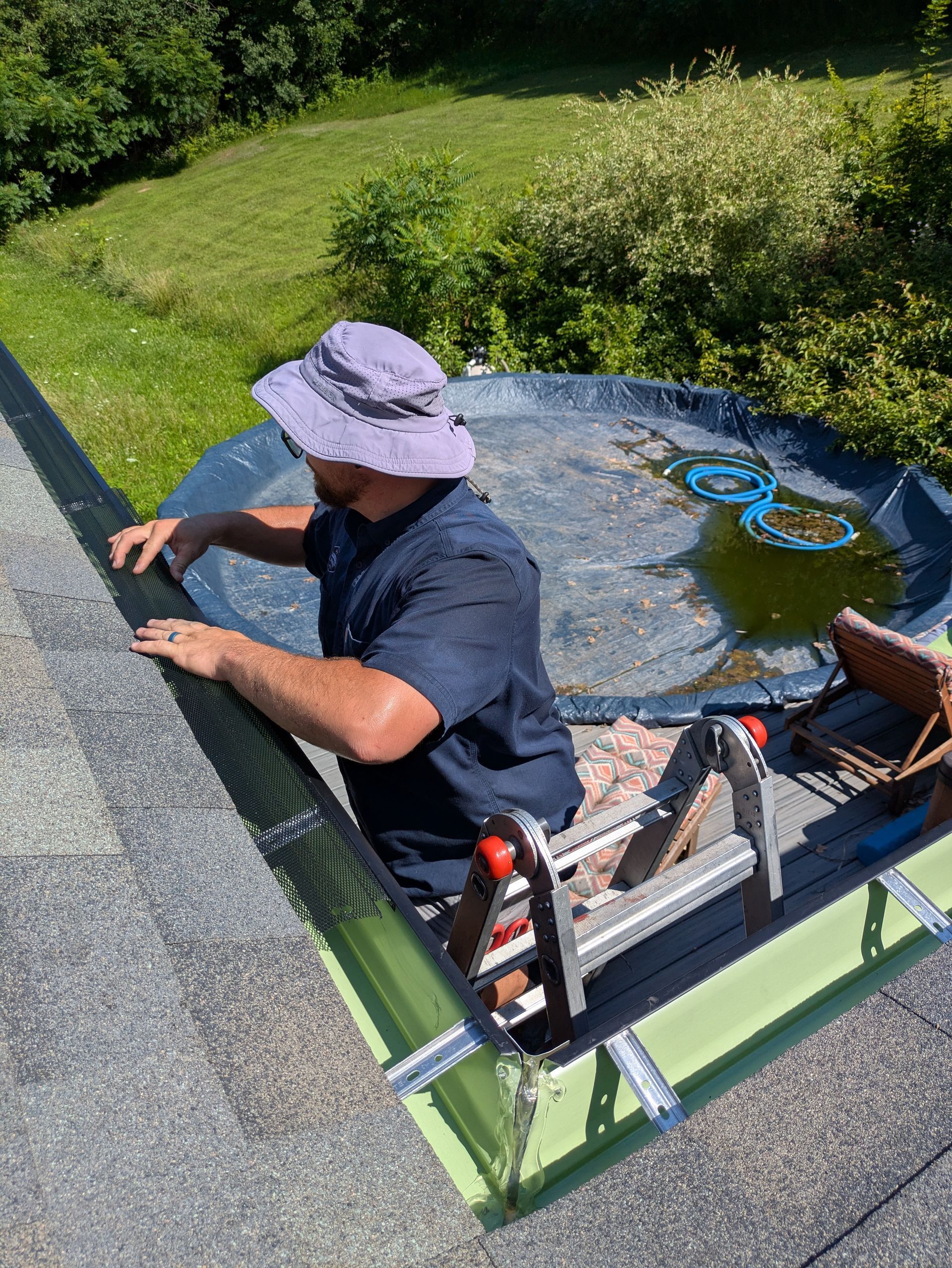 A man is sitting on a ladder fixing a gutter on a roof.