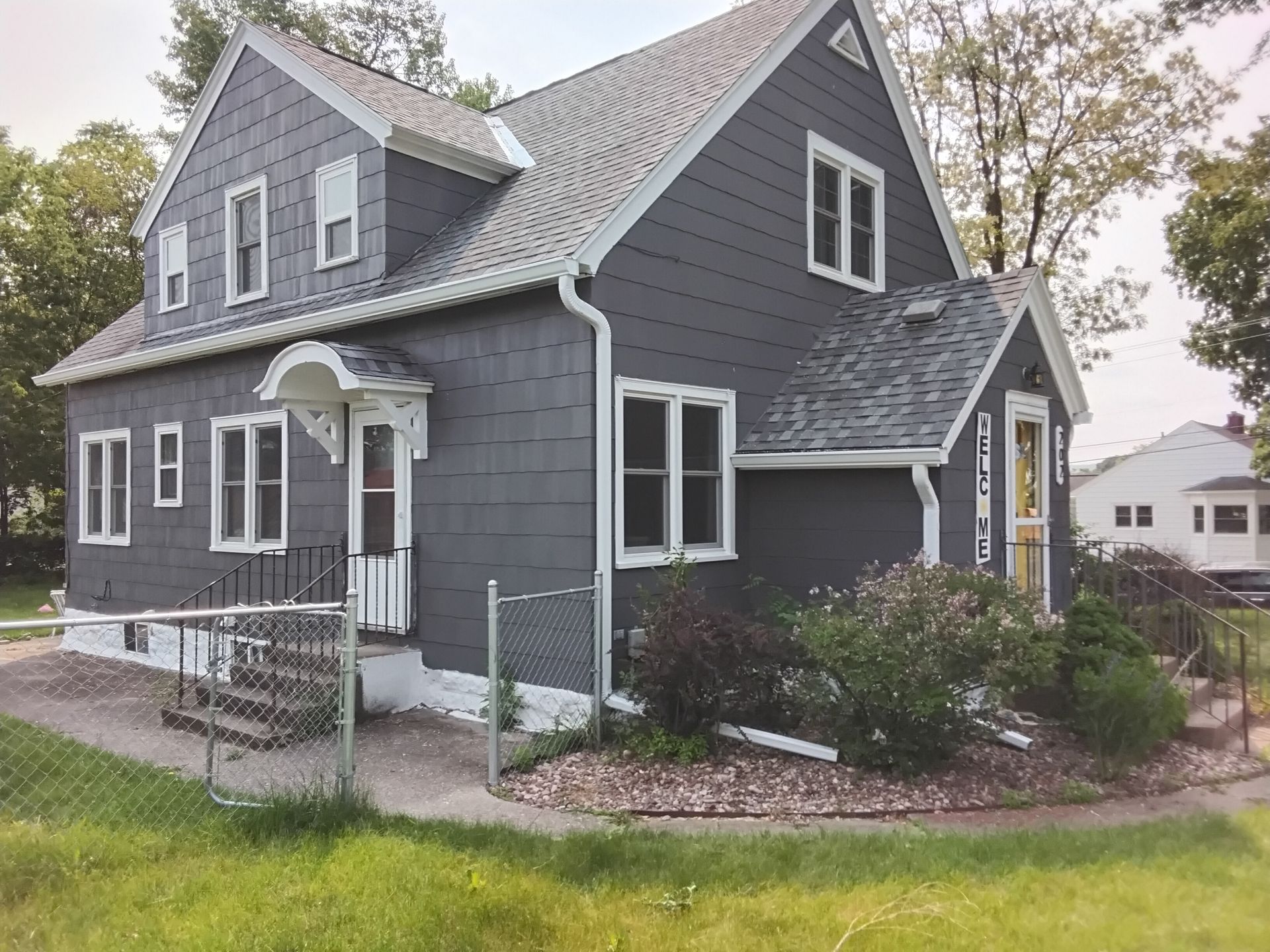 A gray house with white trim and a fence in front of it