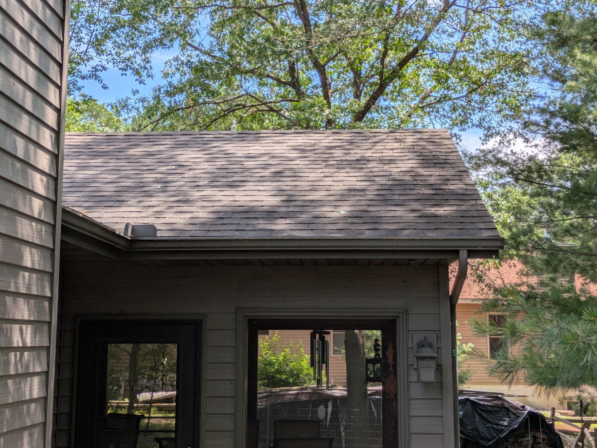A house with a roof that is covered in shingles and trees in the background.