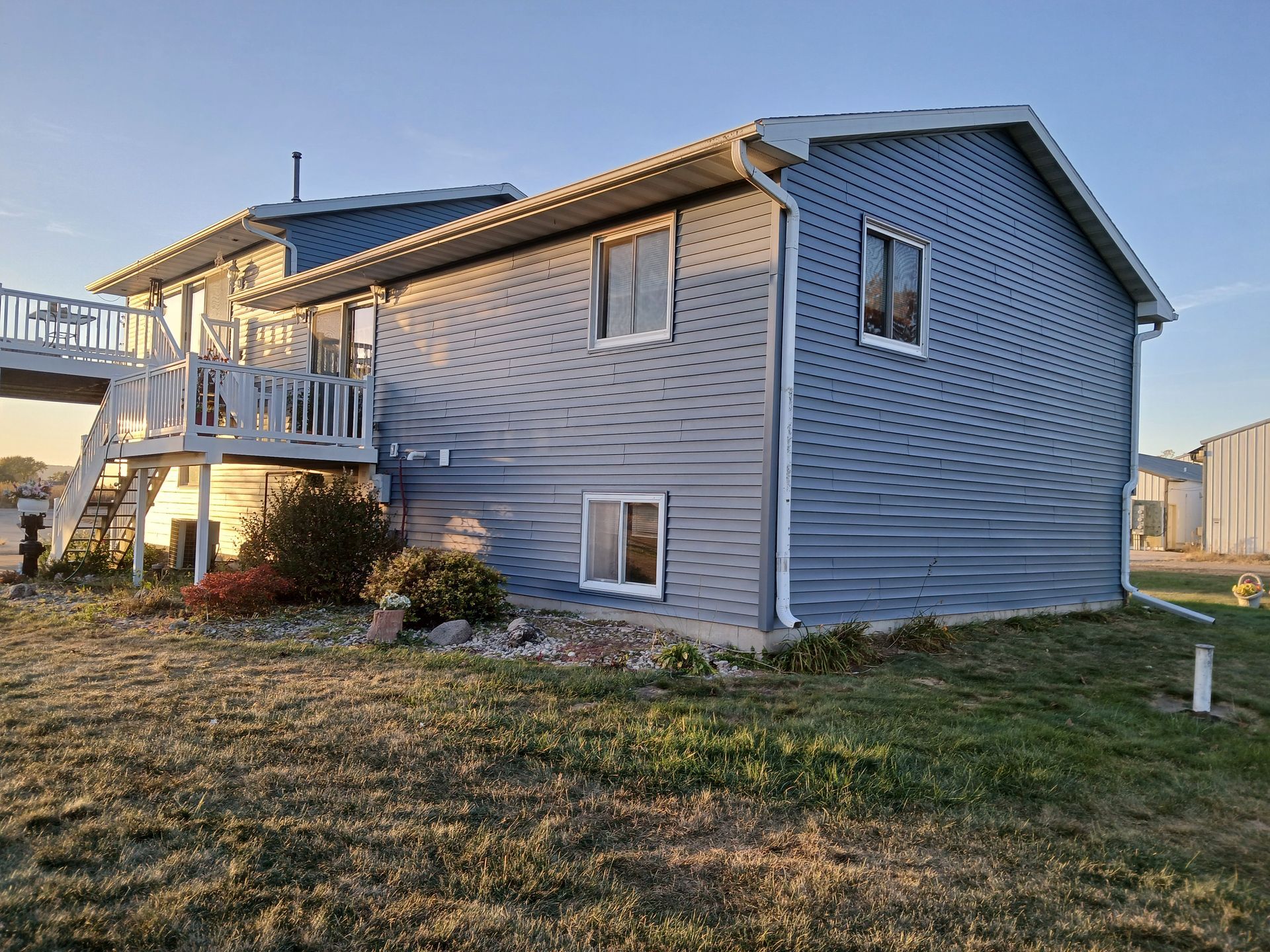 A large house with a deck and stairs is sitting in the middle of a grassy field.