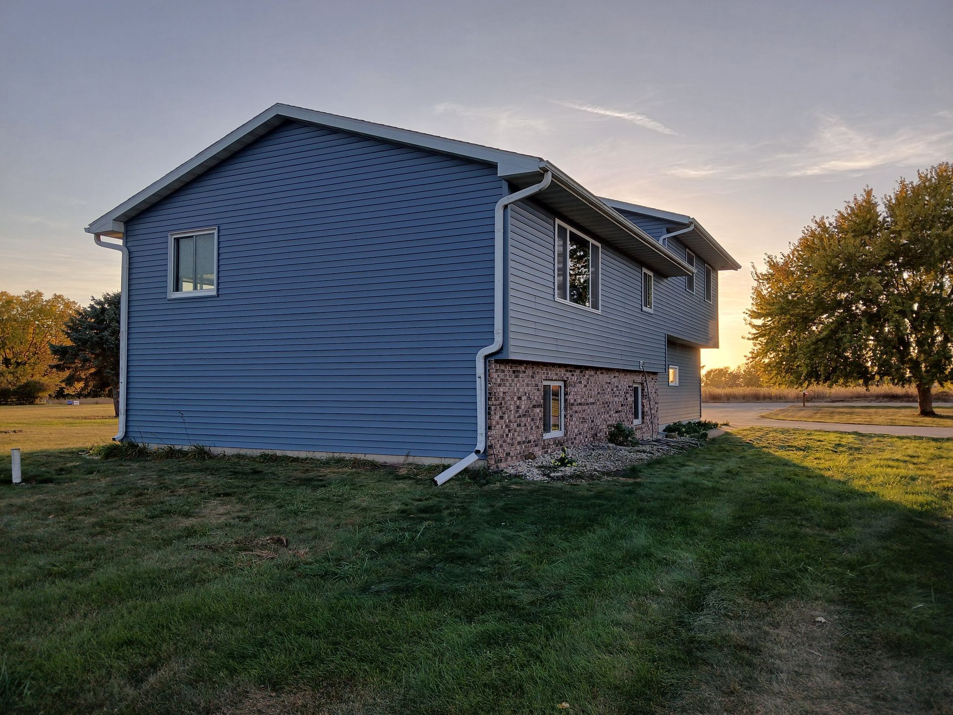 A blue house with a lot of windows is sitting on top of a lush green field.
