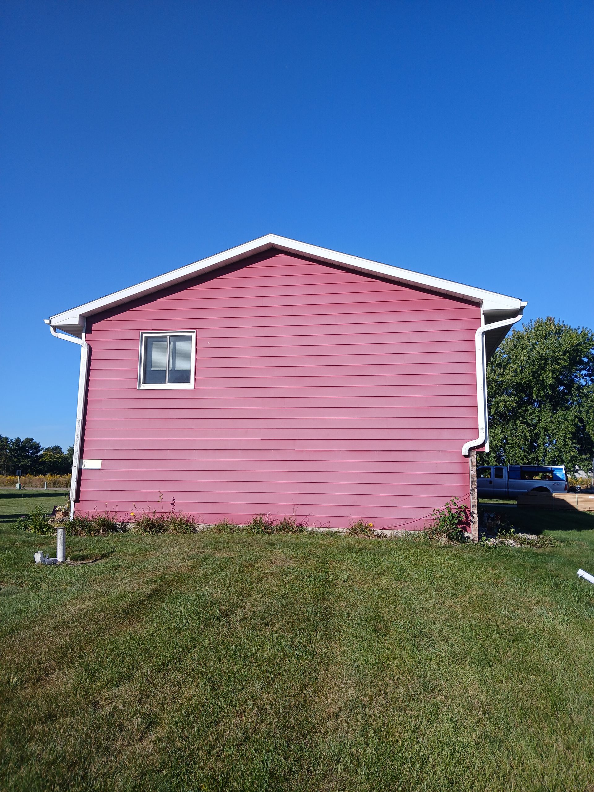 A pink house with a white roof is sitting on top of a lush green field.