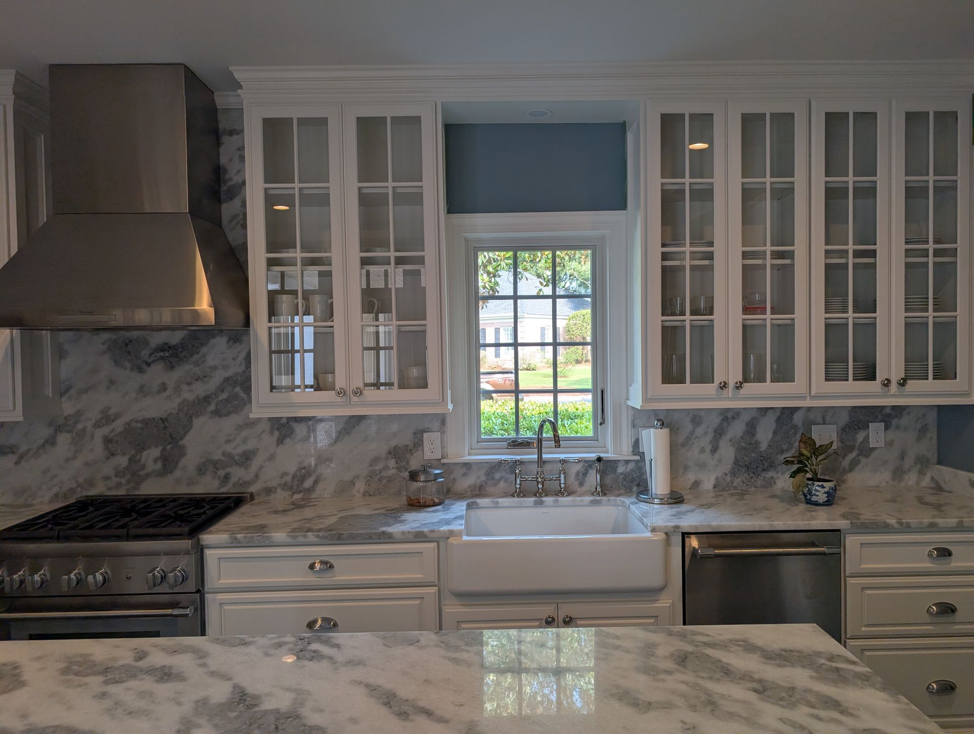 Kitchen with white cabinets, stainless steel range hood, marble countertops, and a window.