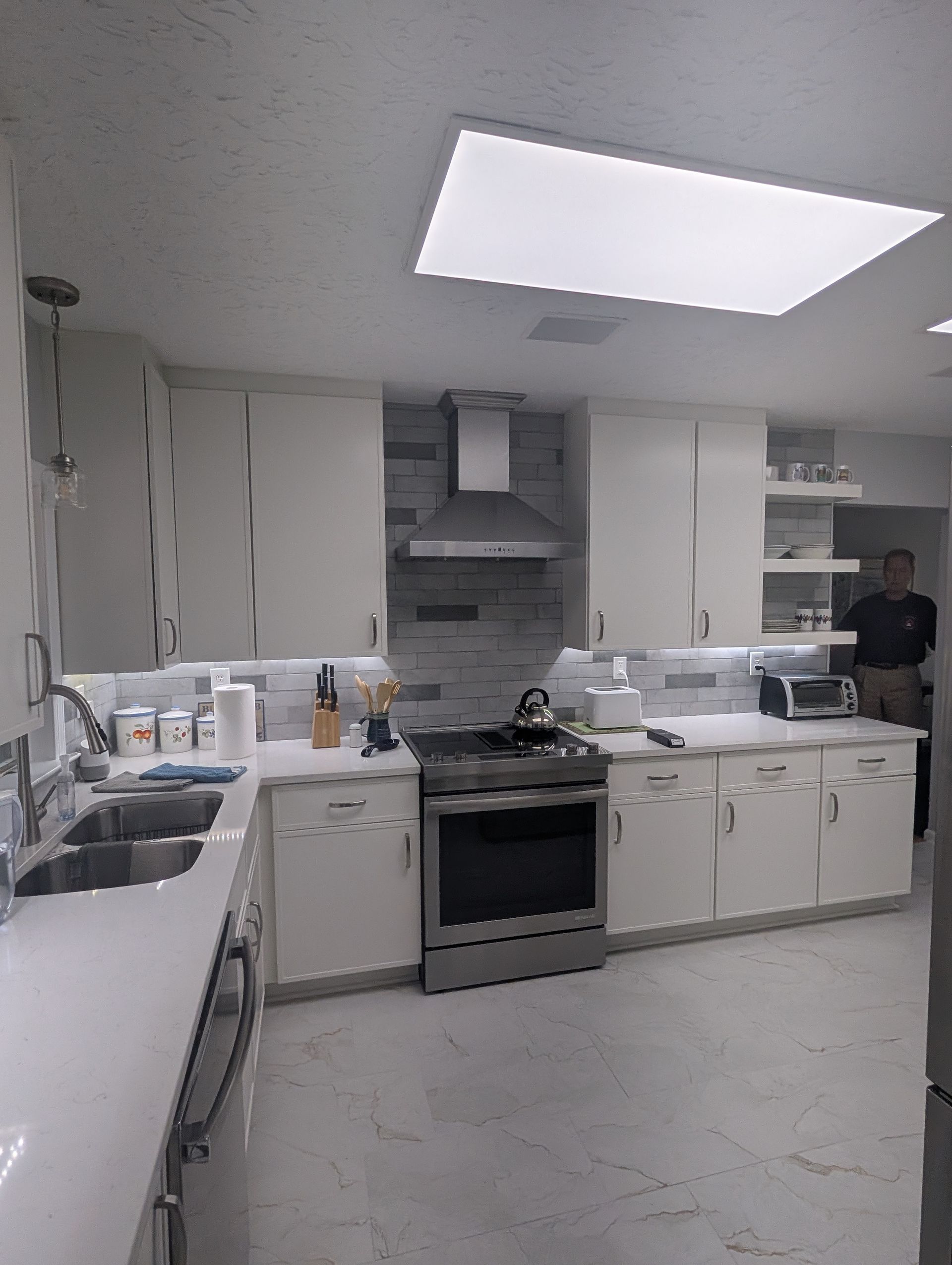 White kitchen with stainless steel appliances and overhead lighting.