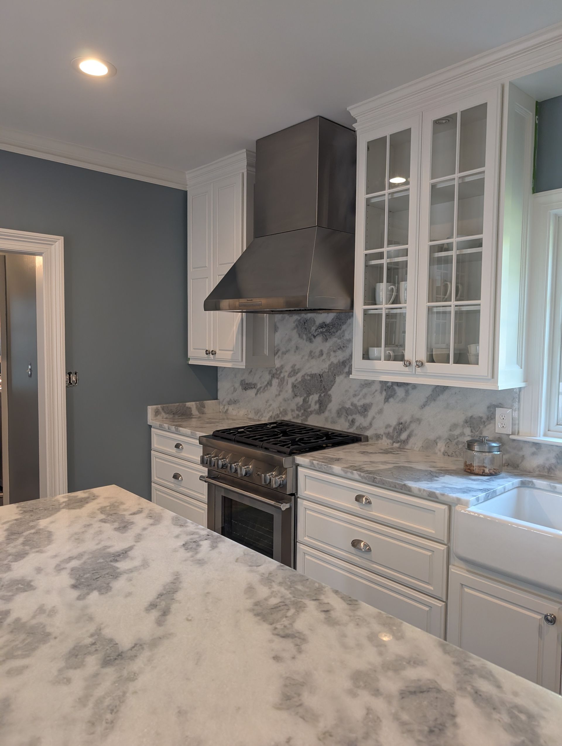 Kitchen with white cabinets, marble countertops, stainless steel range hood, and blue wall.