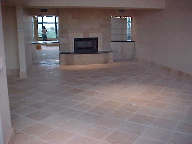 Empty room with beige tiled floor and fireplace, light coming in from outside window.