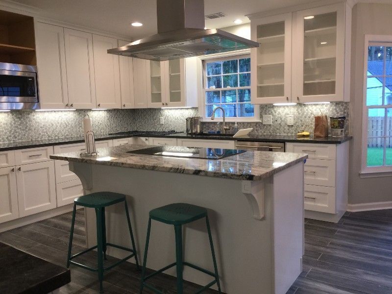 White kitchen with island, stainless steel range hood, glass-front cabinets, and teal stools.