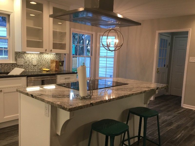 Kitchen with a granite countertop island, stainless steel range hood, white cabinets, and green stools.