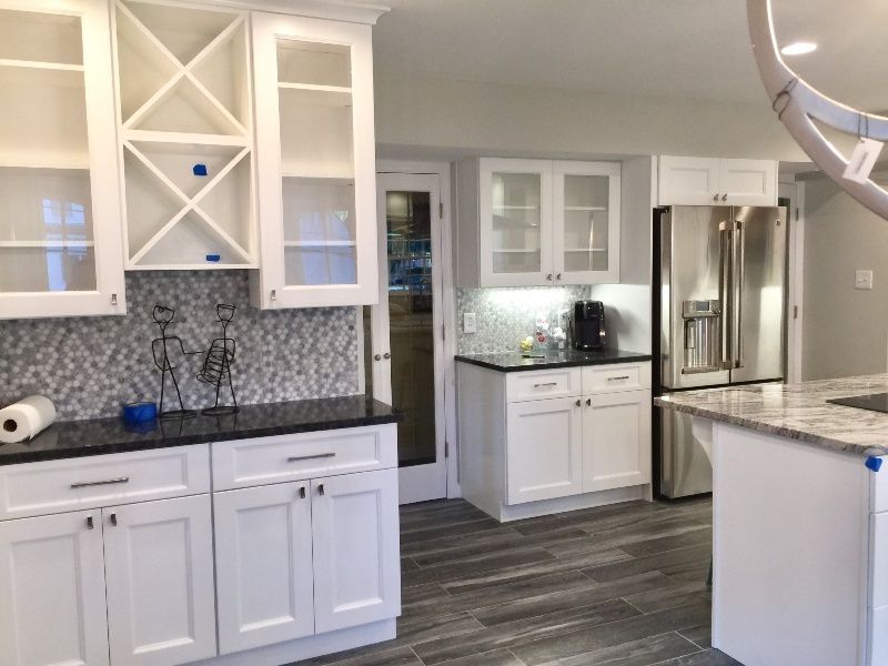White kitchen cabinets with black countertops and gray tile backsplash.