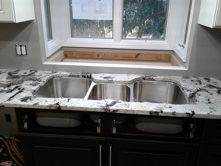 Kitchen with triple sink, granite countertop, dark cabinets, and window above.