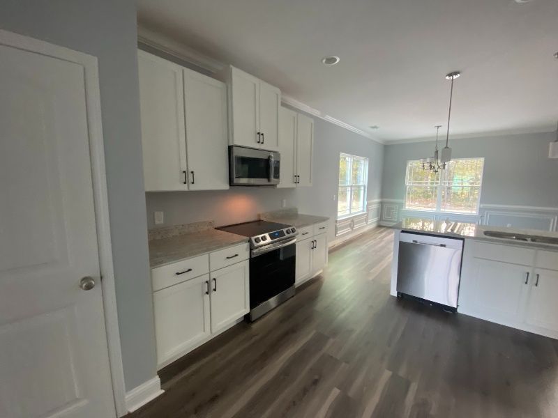 White kitchen with stainless steel appliances, light gray walls, and wood-look flooring.