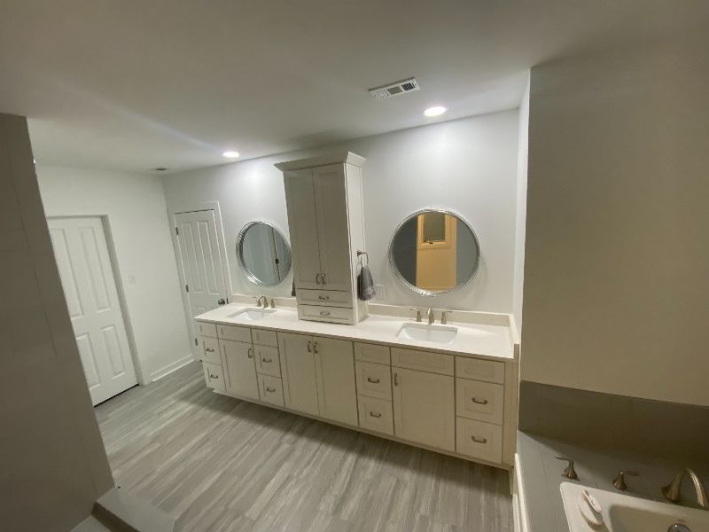 Bathroom with double vanity, two round mirrors, and storage cabinet, all in neutral tones.
