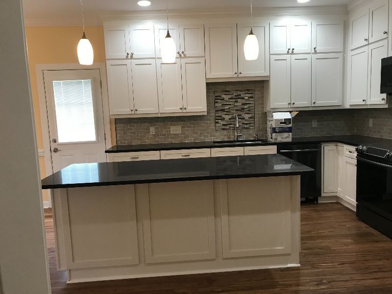 White kitchen with black countertops and island, pendant lights, wooden floor, and backsplash.