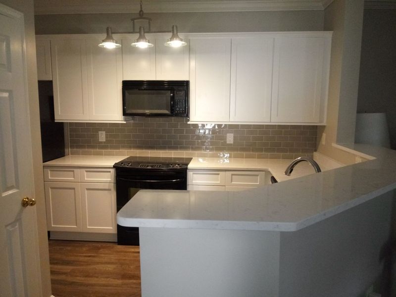 White kitchen with black appliances, a tile backsplash, and a breakfast bar.