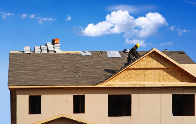 Roofers working on a house roof under a blue sky with clouds