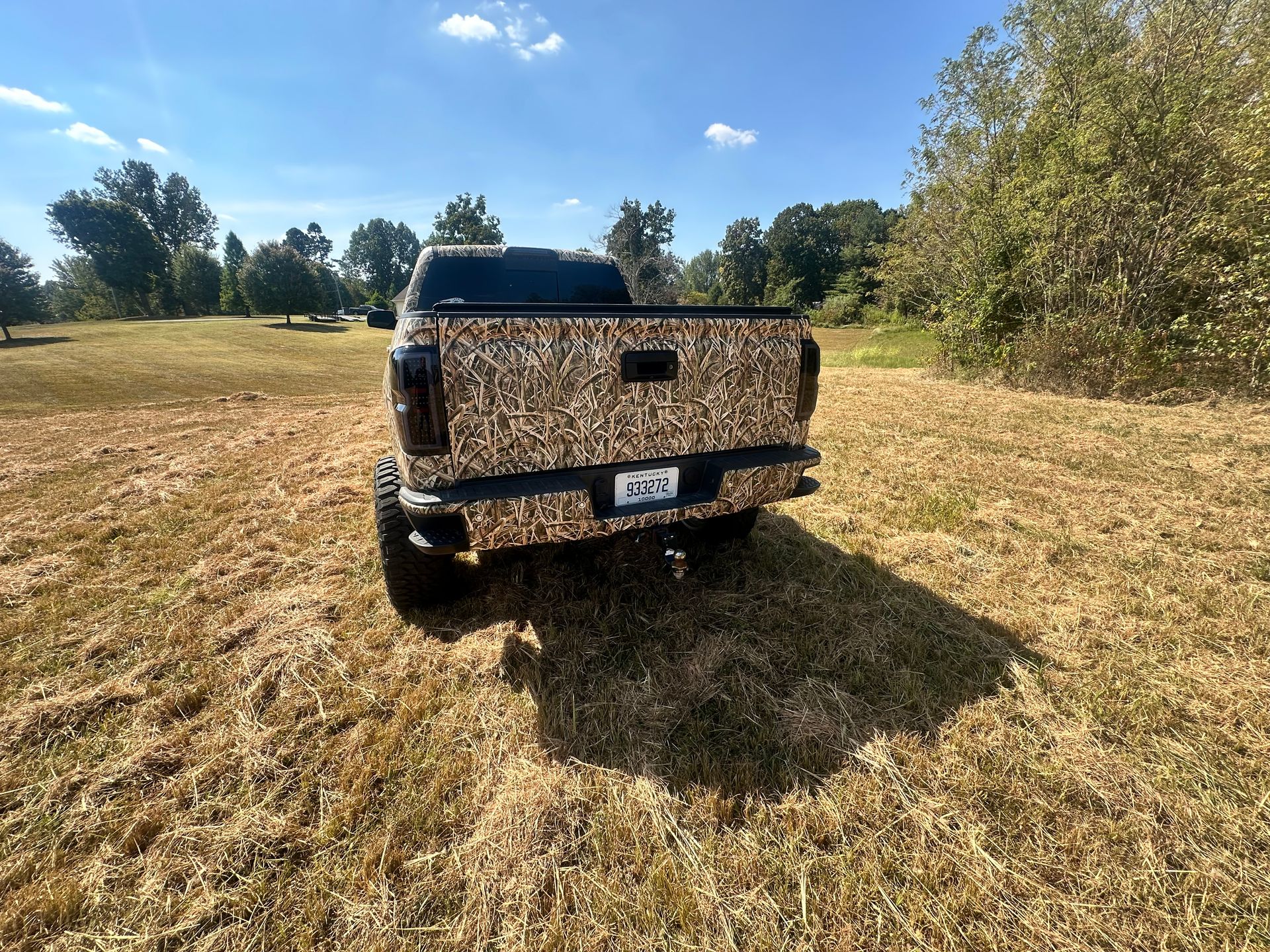Rear view of a camouflage pickup truck parked in a grassy field on a sunny day.