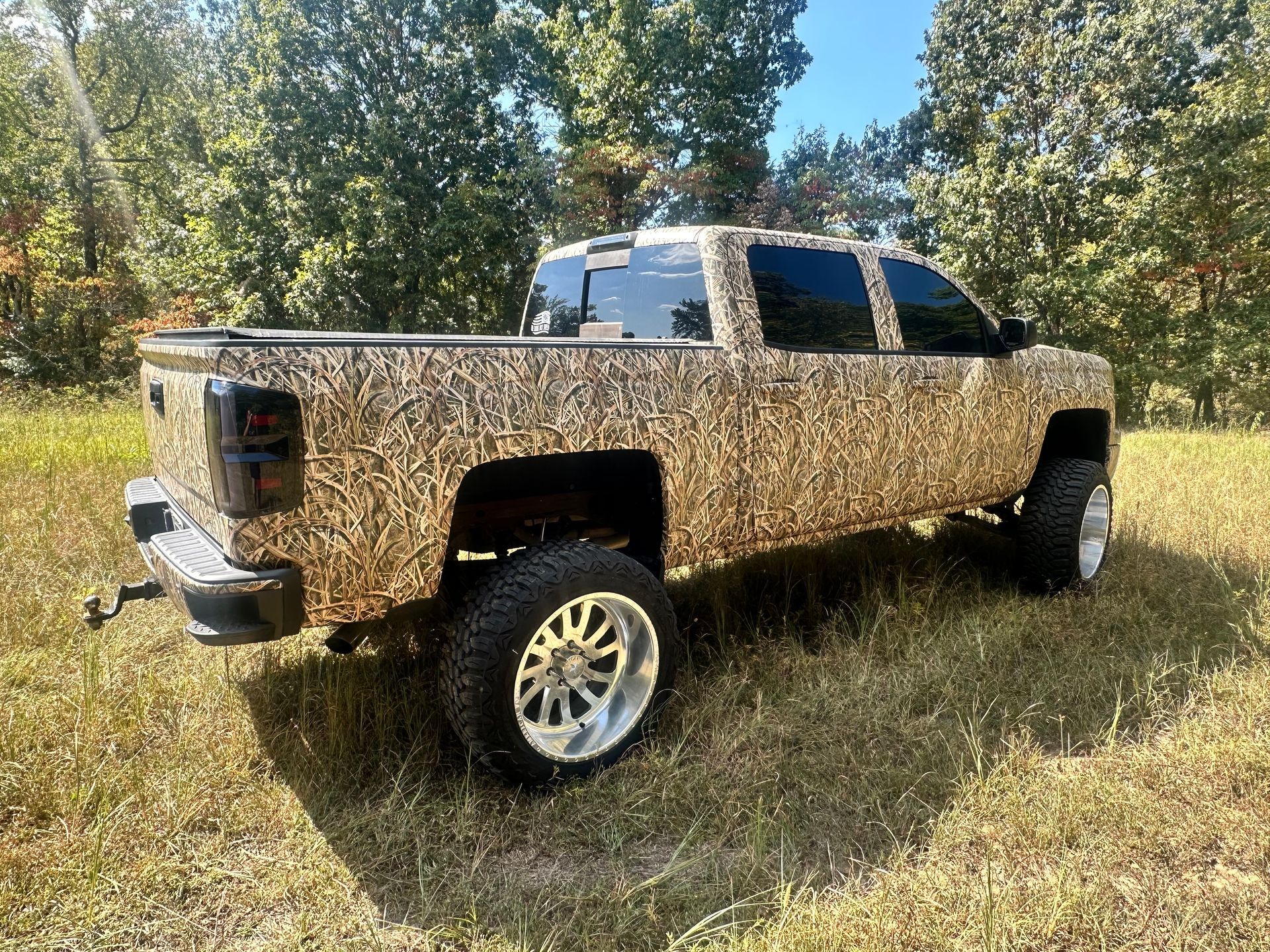 Camouflage pickup truck with large chrome rims parked in a grassy field.