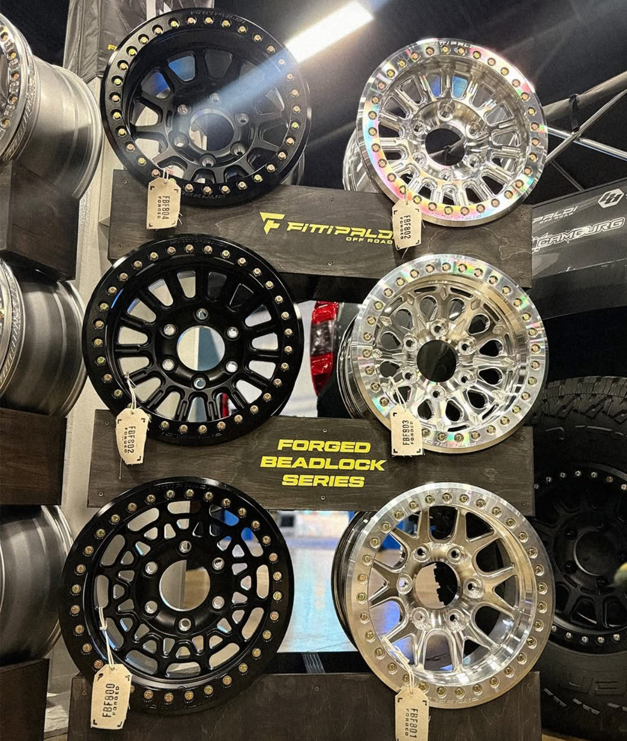 Display of black and silver forged beadlock wheels in a showroom setting.