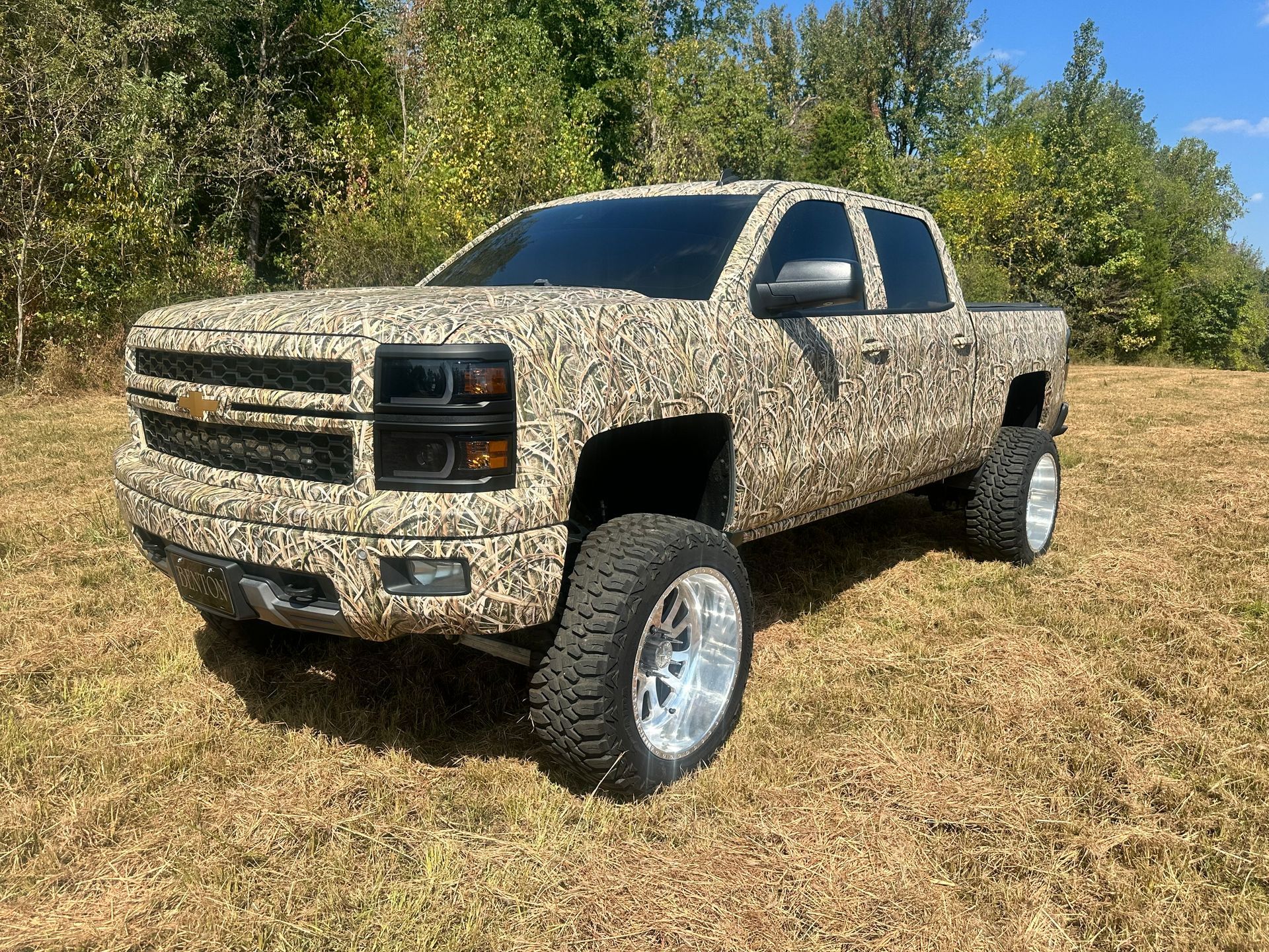 Camouflage Chevy truck parked on a grassy field with trees in the background.