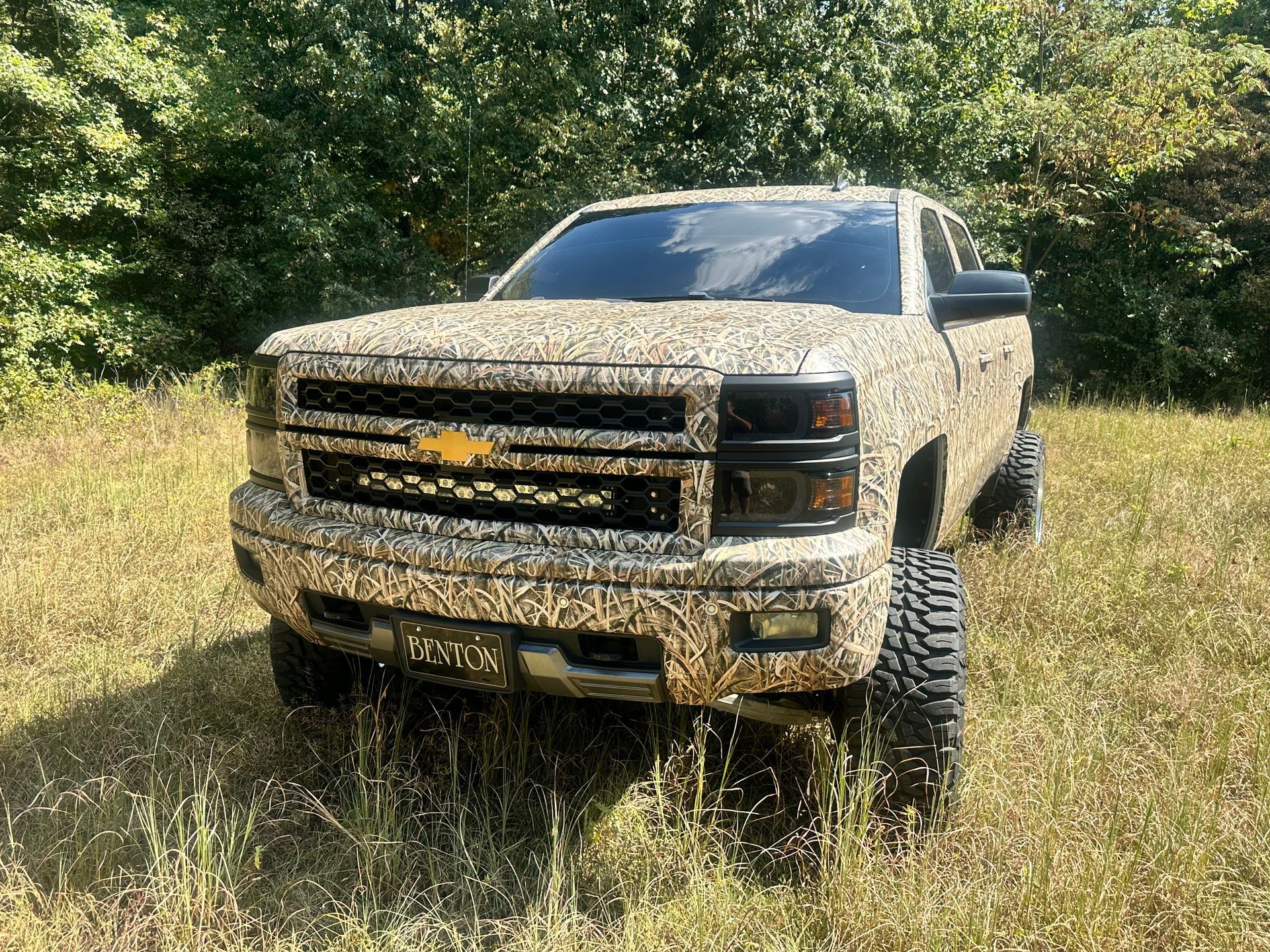 Camouflage Chevy pickup truck in a grassy field.
