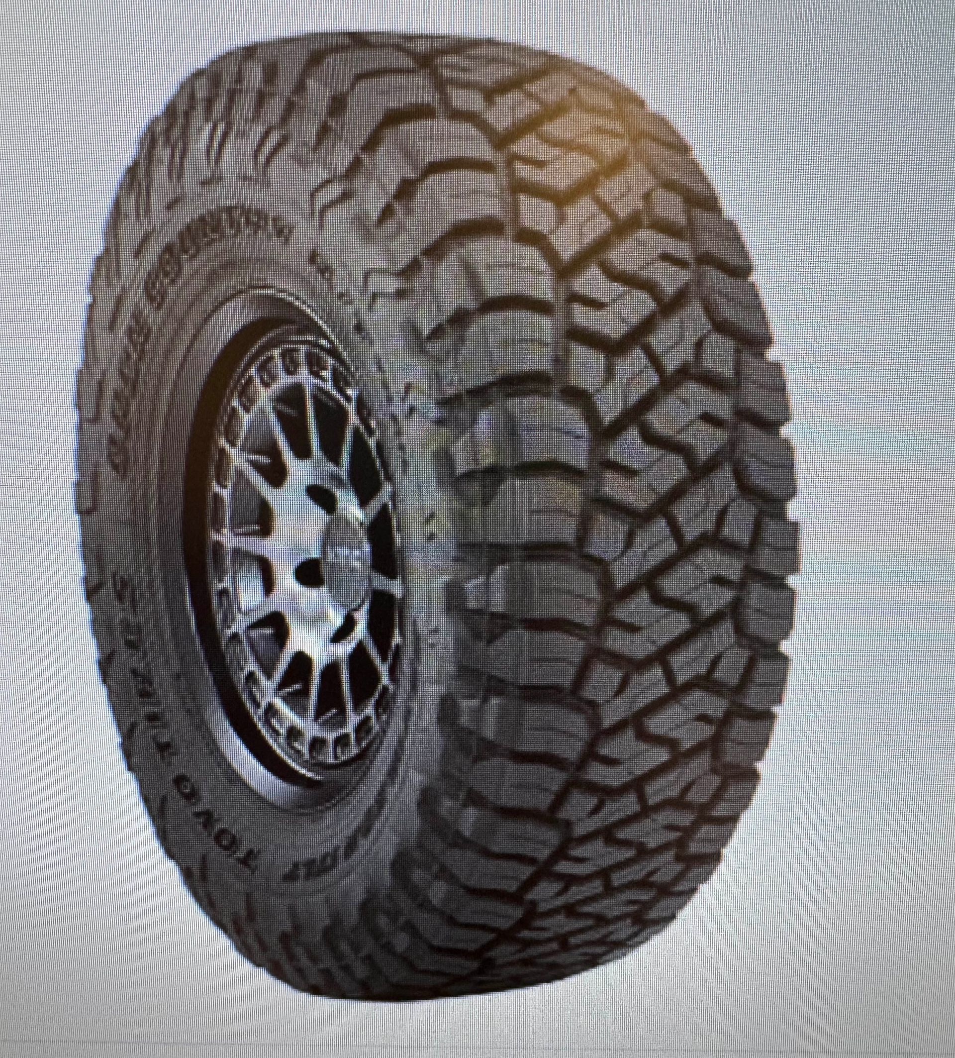 Black off-road tire on a gray and silver rim with deep treads.