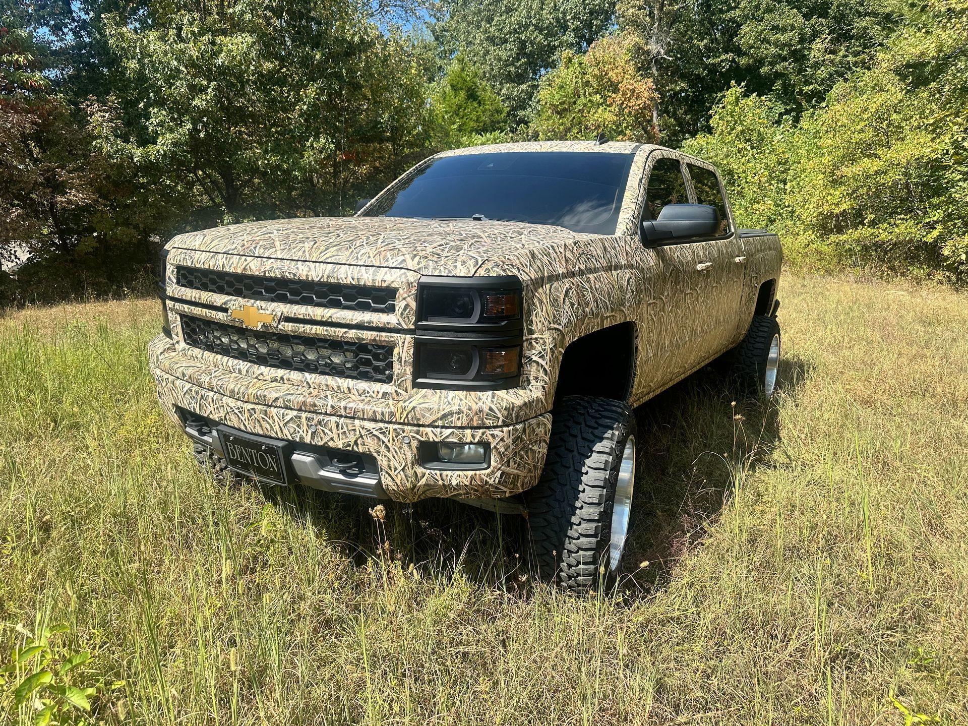 Camouflage-wrapped Chevrolet truck parked in a grassy field on a sunny day.