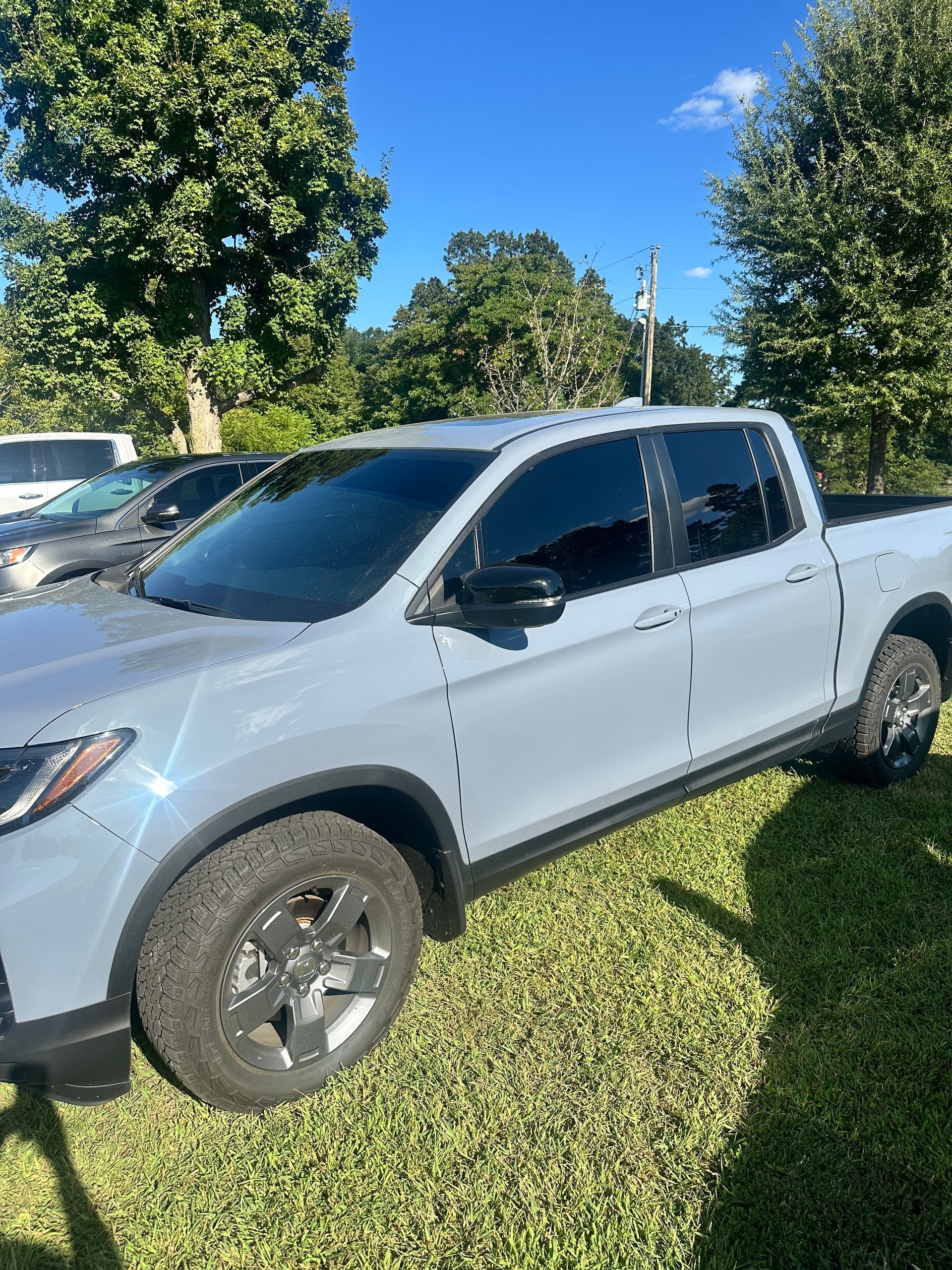 Gray Honda Ridgeline pickup truck on grass with tinted windows, under a blue sky.