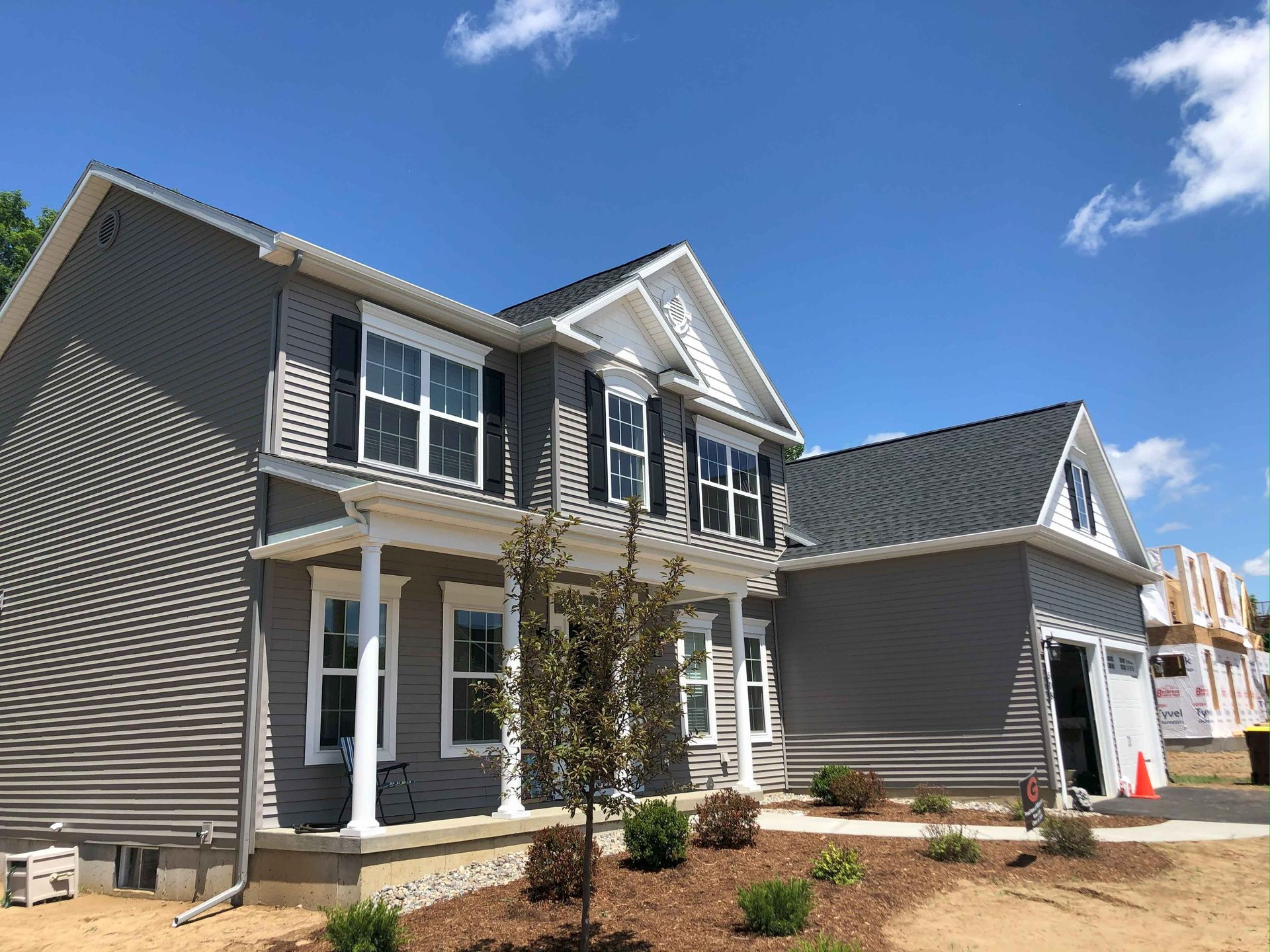 A large gray house with white trim and shutters is being built.