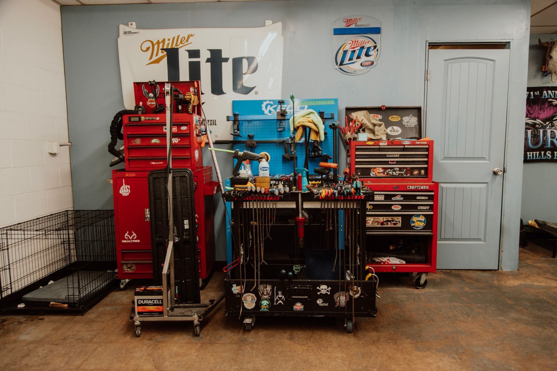 A garage with tool chests, a Miller Lite sign, a blue pegboard, and tools.