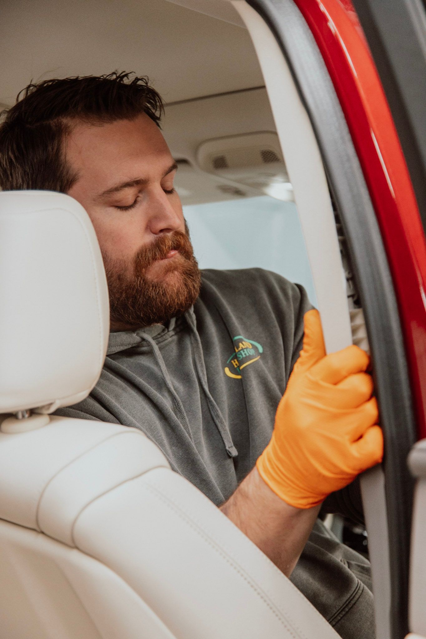 Man in orange gloves works on a car door seal in a vehicle, with a white seat in the foreground.