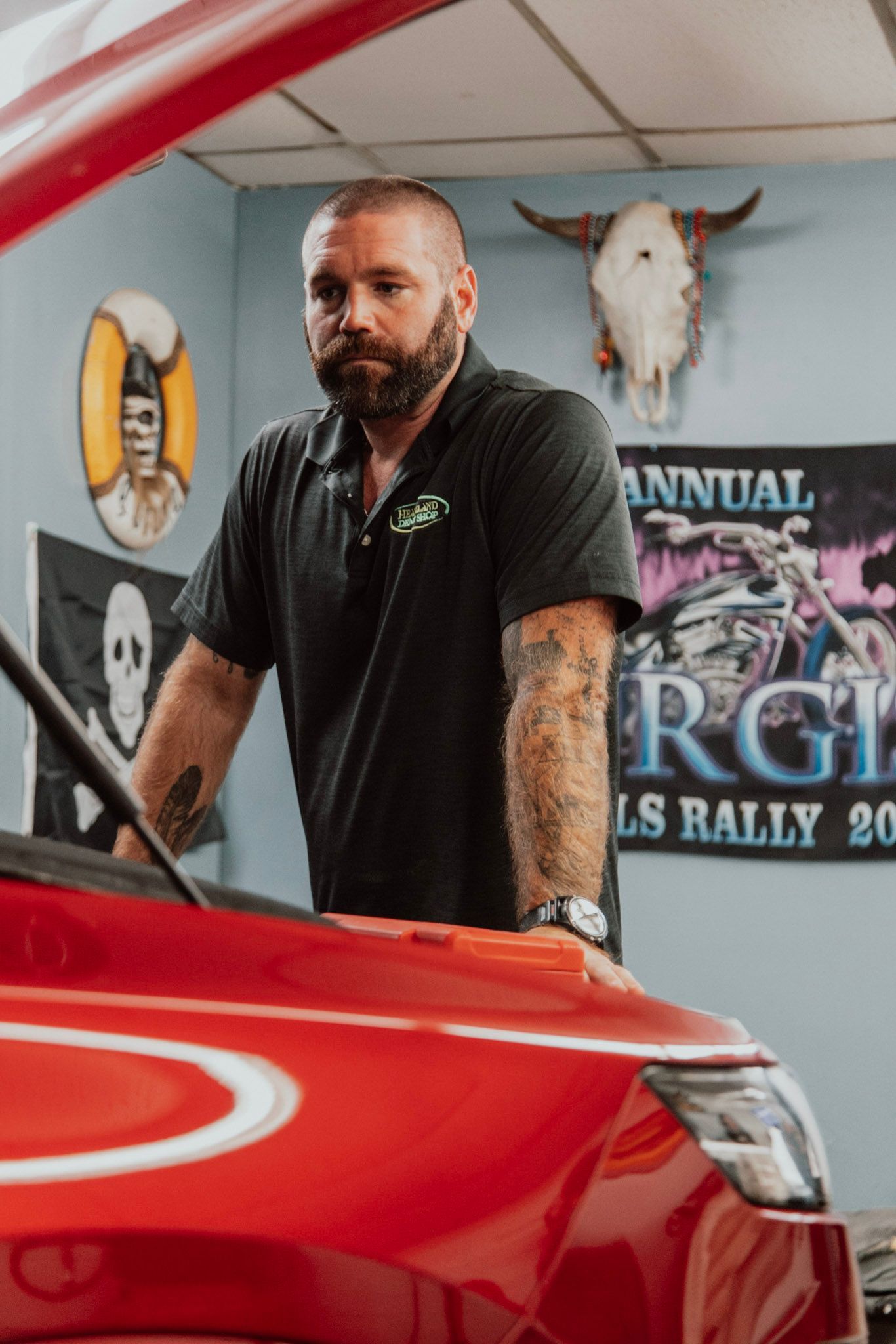 Man with beard looking at car engine in a garage with skull decor.