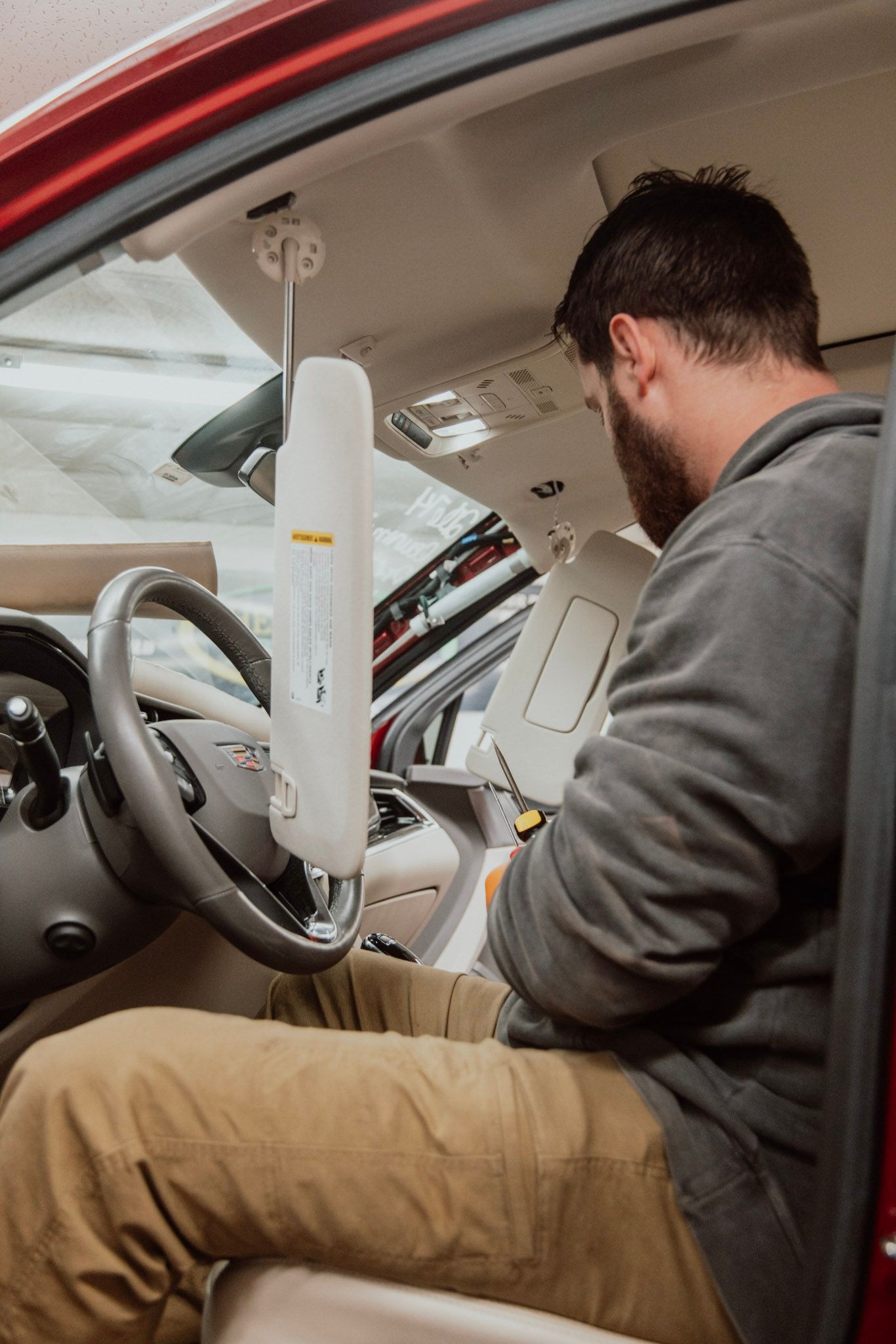 Man inside red car working, holding device, with steering wheel, visor and dashboard visible.