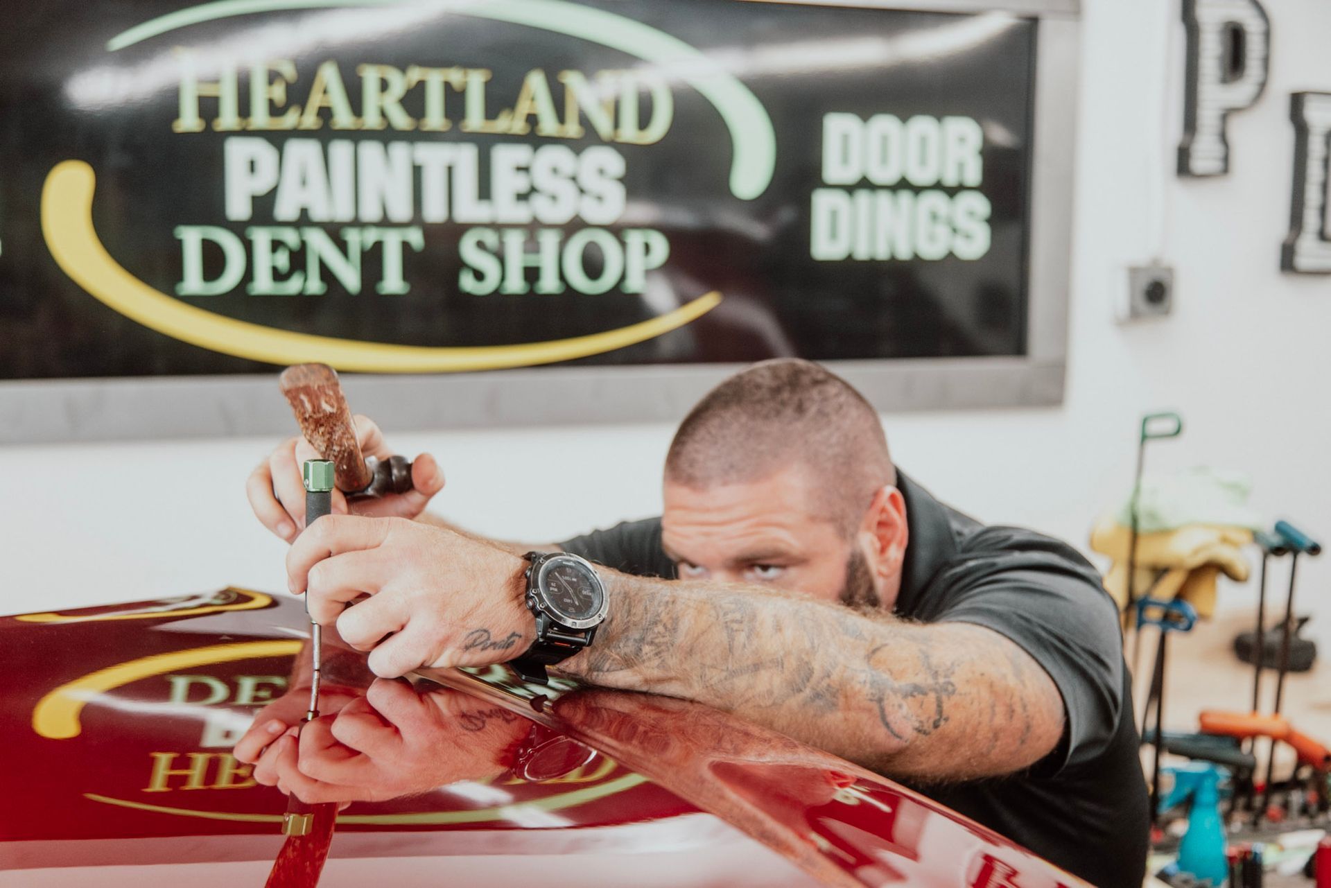 Man working on a car, Heartland Paintless Dent Shop sign in background.