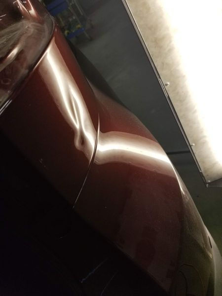 Red car panel with a dent, illuminated by overhead light.