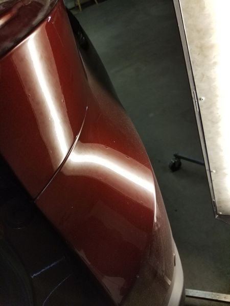 Dark red car body with a dent, under bright lights in a garage.