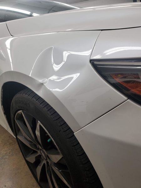 White car with a dent on the front fender above the wheel.