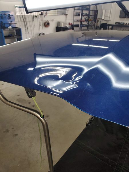 Blue car hood with several dents, being repaired in a garage with bright overhead lights.