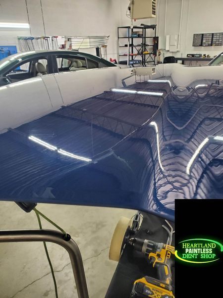 Blue car hood reflecting workshop lights, being detailed.