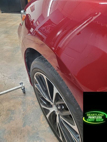 Red car fender with a dent, wheel visible, logo of 