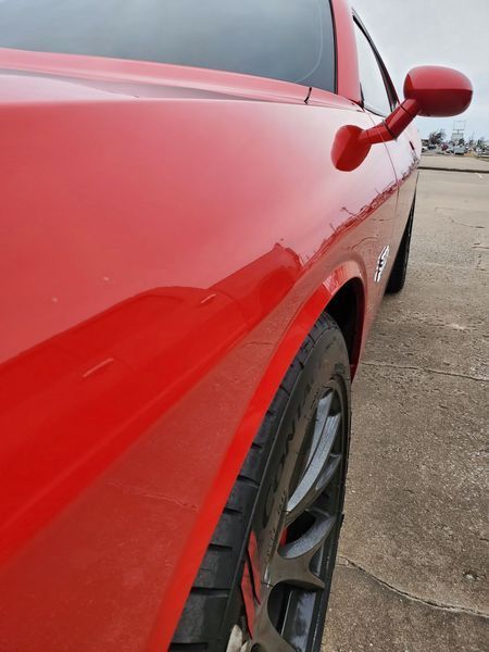 Red Dodge Challenger car, close up of side panel and wheel, outdoors on a cloudy day.