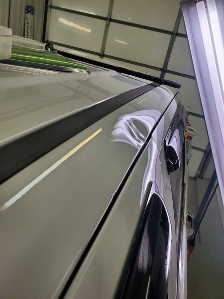 Silver car roof with a dent under inspection lights.