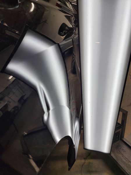 Dent in shiny car panel, reflecting light and showing the damage.