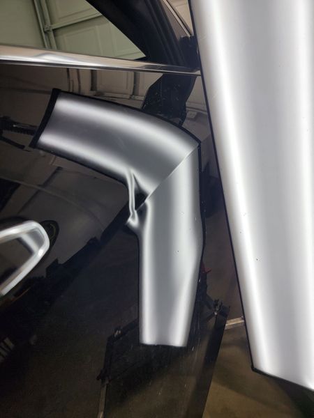 Black car panel with dent, highlighted by reflection from light.