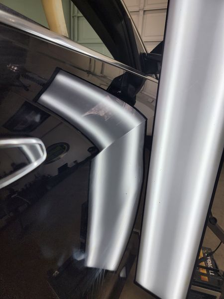 Car dent repair in progress: angled reflections reveal damage on a black car door.