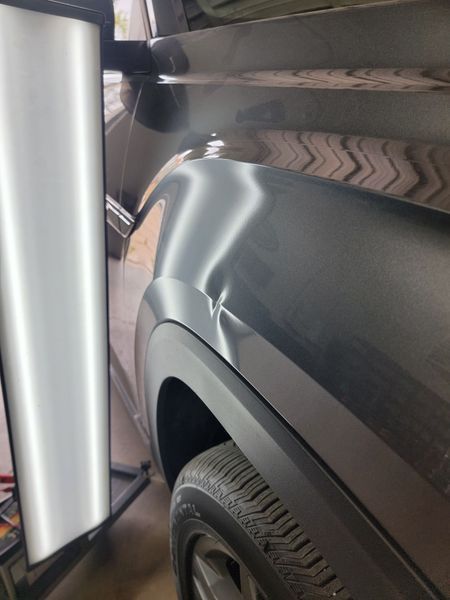 Dark gray car fender with dent being worked on near wheel.