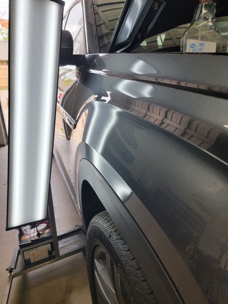 A dented, dark-colored car fender being repaired using a reflection board.
