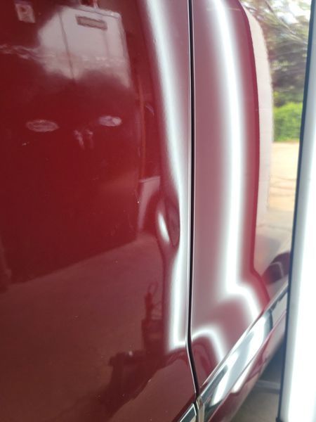 Red car door with a dent. Light reflection highlights the damage and body lines.